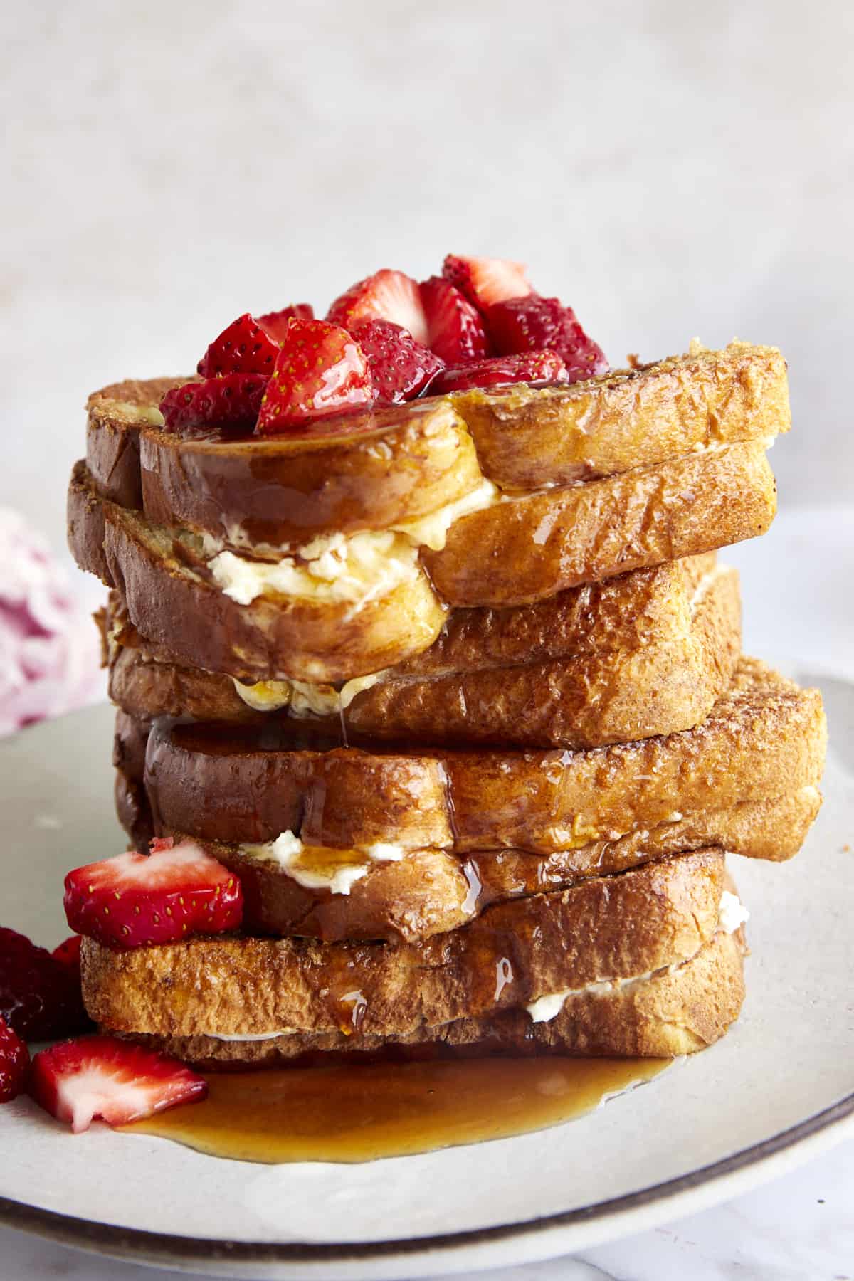 Cream cheese stuffed air fryer french toast sandwiches stacked on top of each other topped with berries and syrup. 