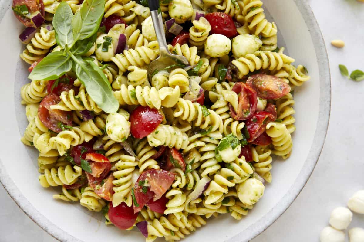 A fork sinking into a bowl of pasta salad with pesto. 