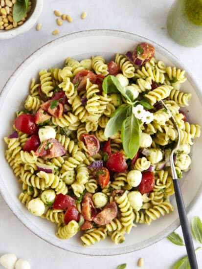 A bowl of pasta salad with pesto with a fork on the side.