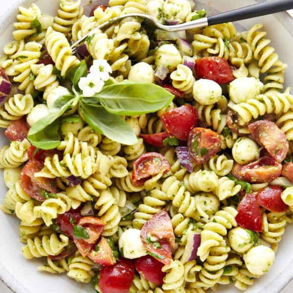 A bowl of pasta salad with pesto topped with fresh basil.