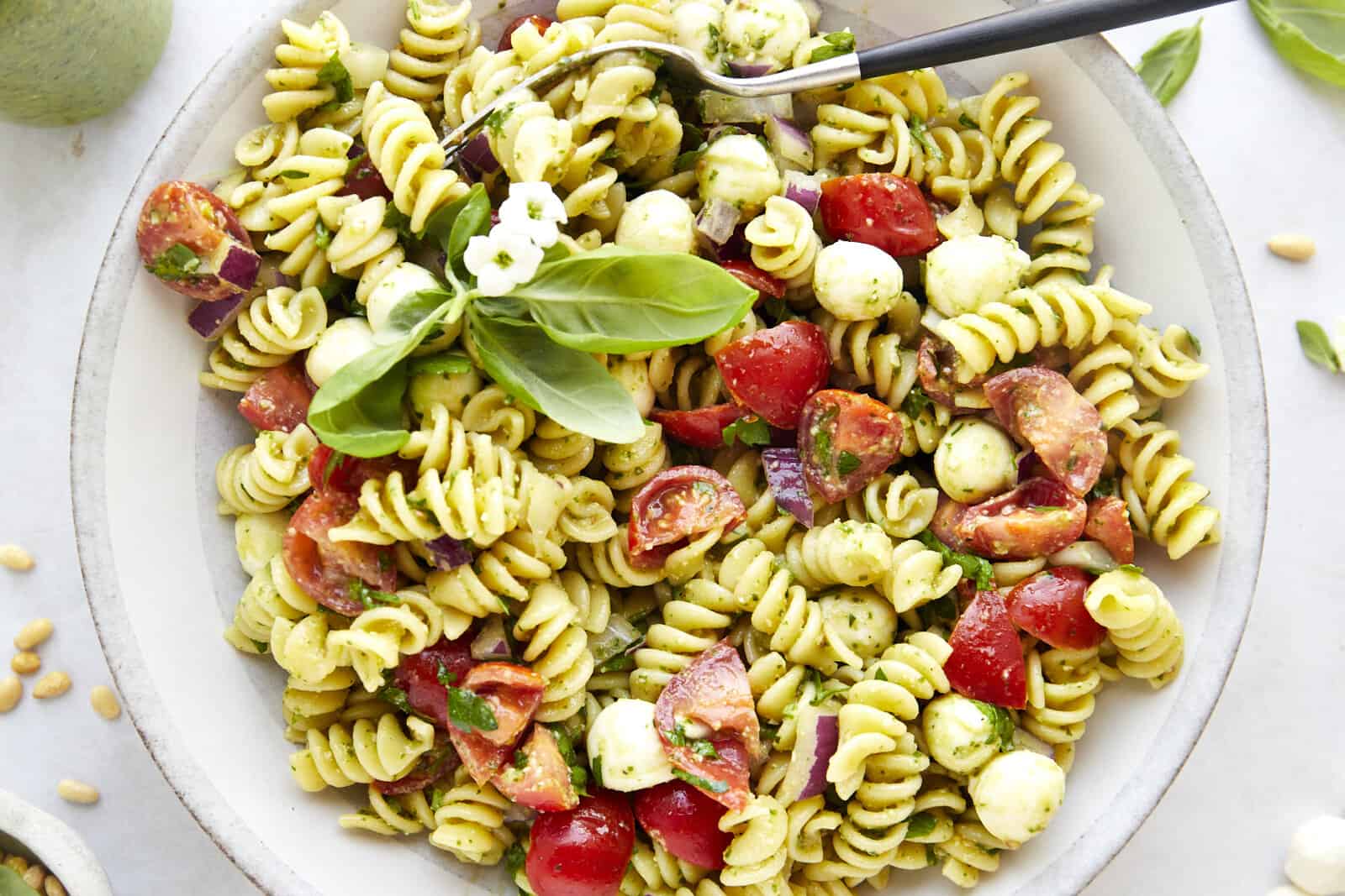 A bowl of pasta salad with pesto topped with fresh basil.