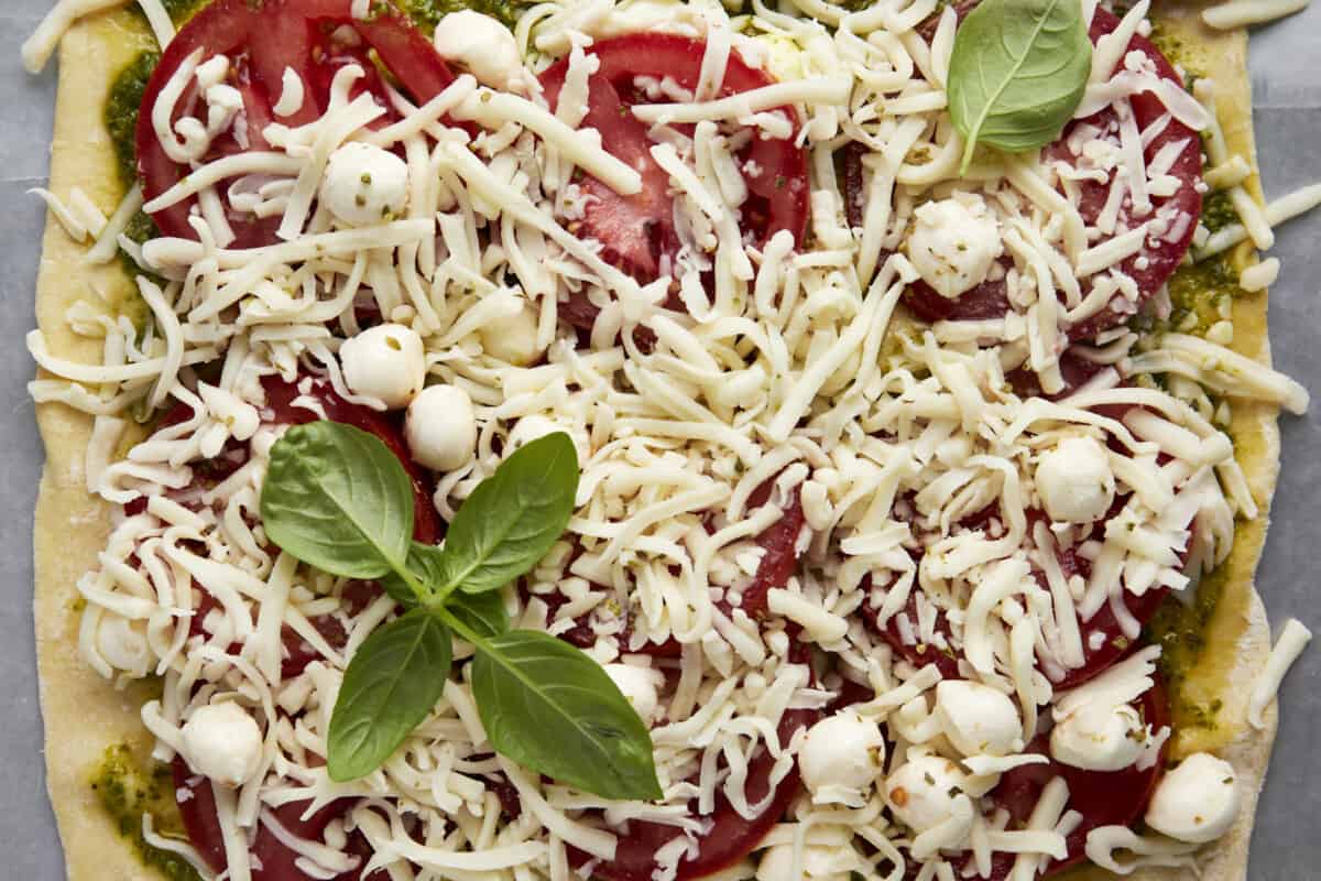 Unbaked puff pastry topped with pesto, tomatoes, Mozzarella pearls, shredded Mozzarella, and basil. 