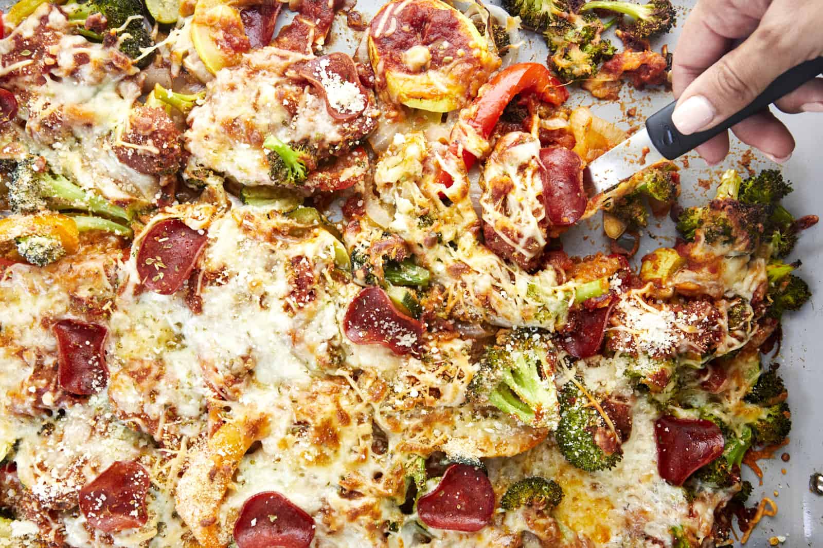 A hand slicing a portion of veggie pizza bake.