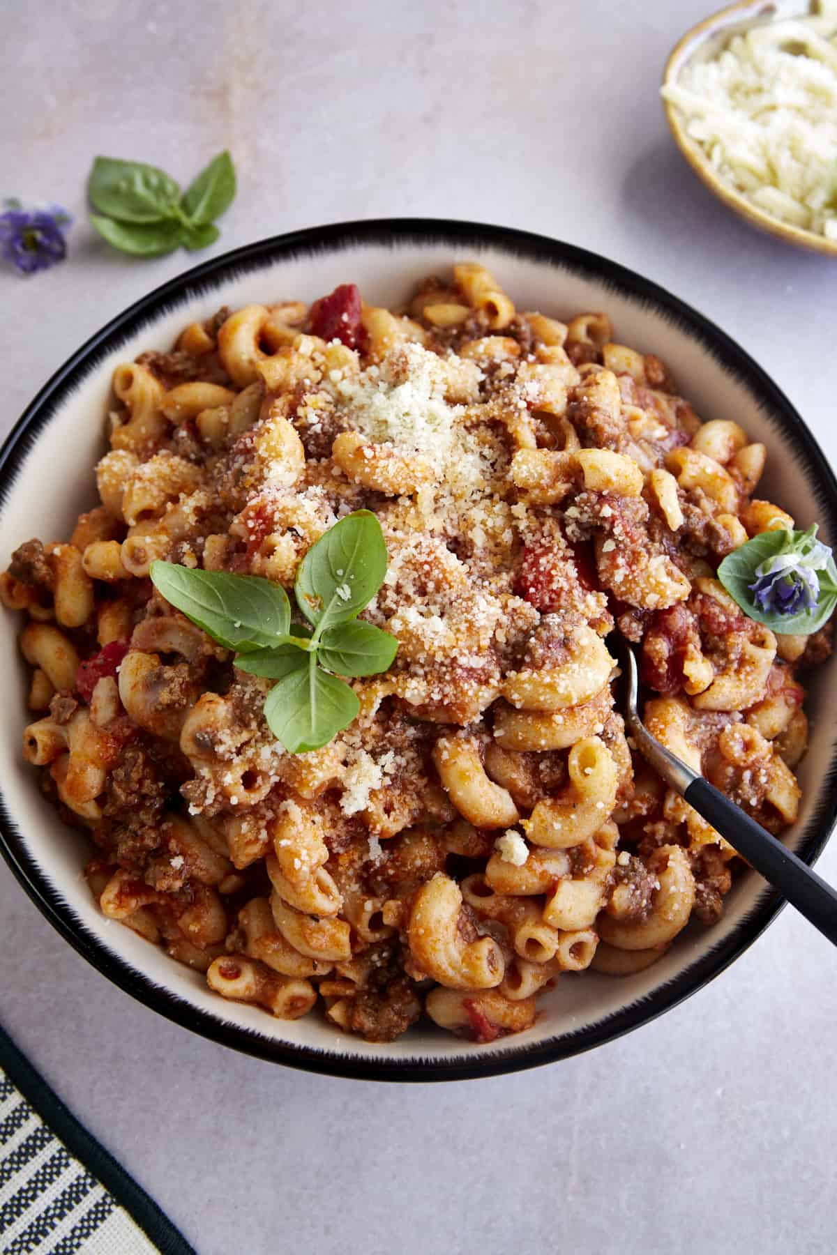 A bowl of ground beef pasta topped with grated Parmesan and fresh parsley with a fork sticking out. 