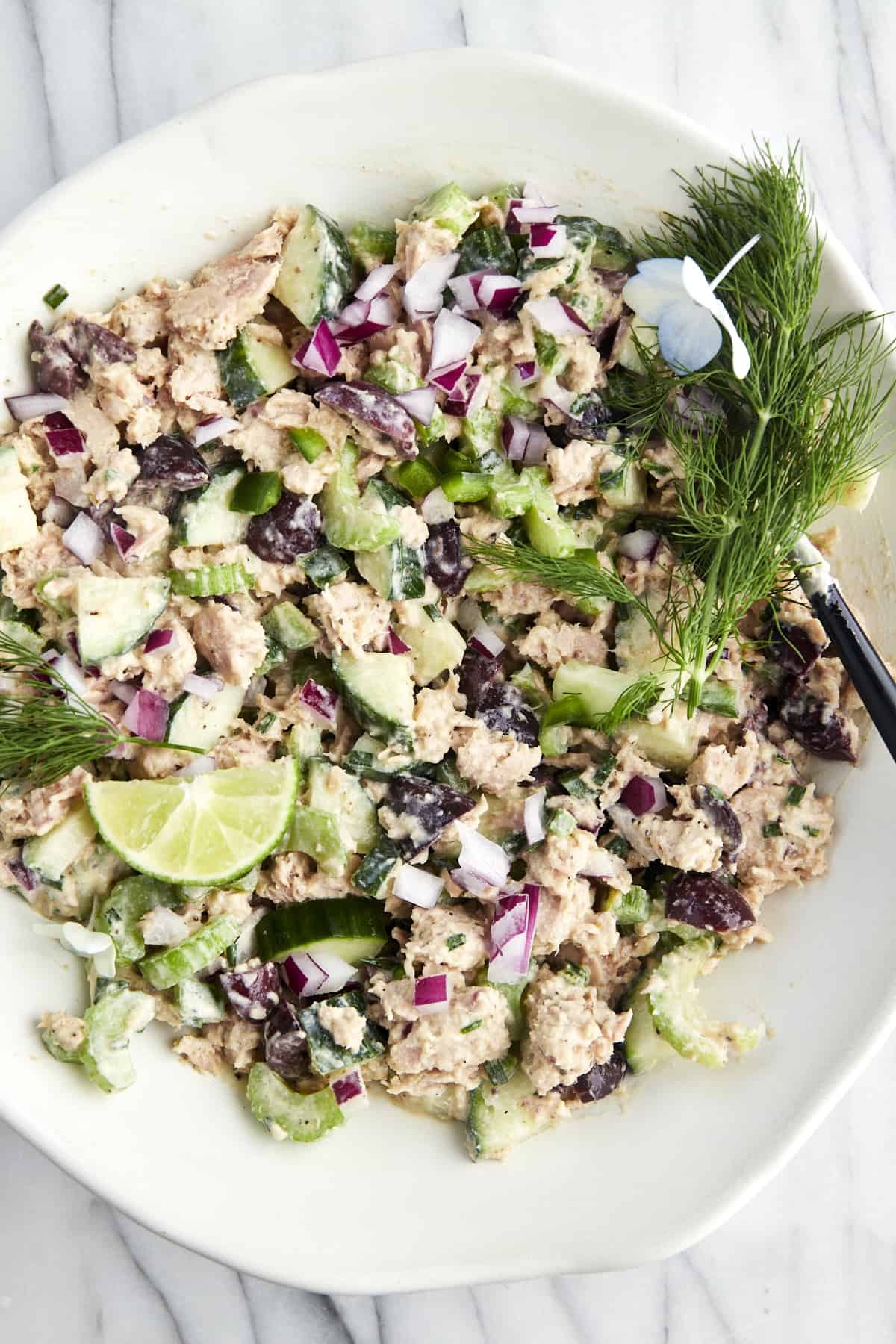 A bowl of Mediterranean tuna salad topped with fresh dill and lime wedges. 