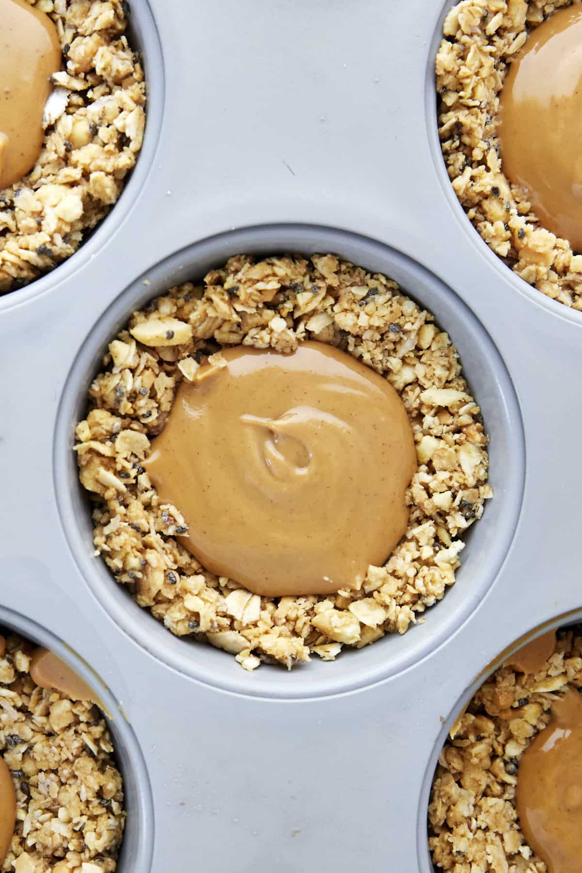 An oat cup in a muffin tin full of peanut butter. 