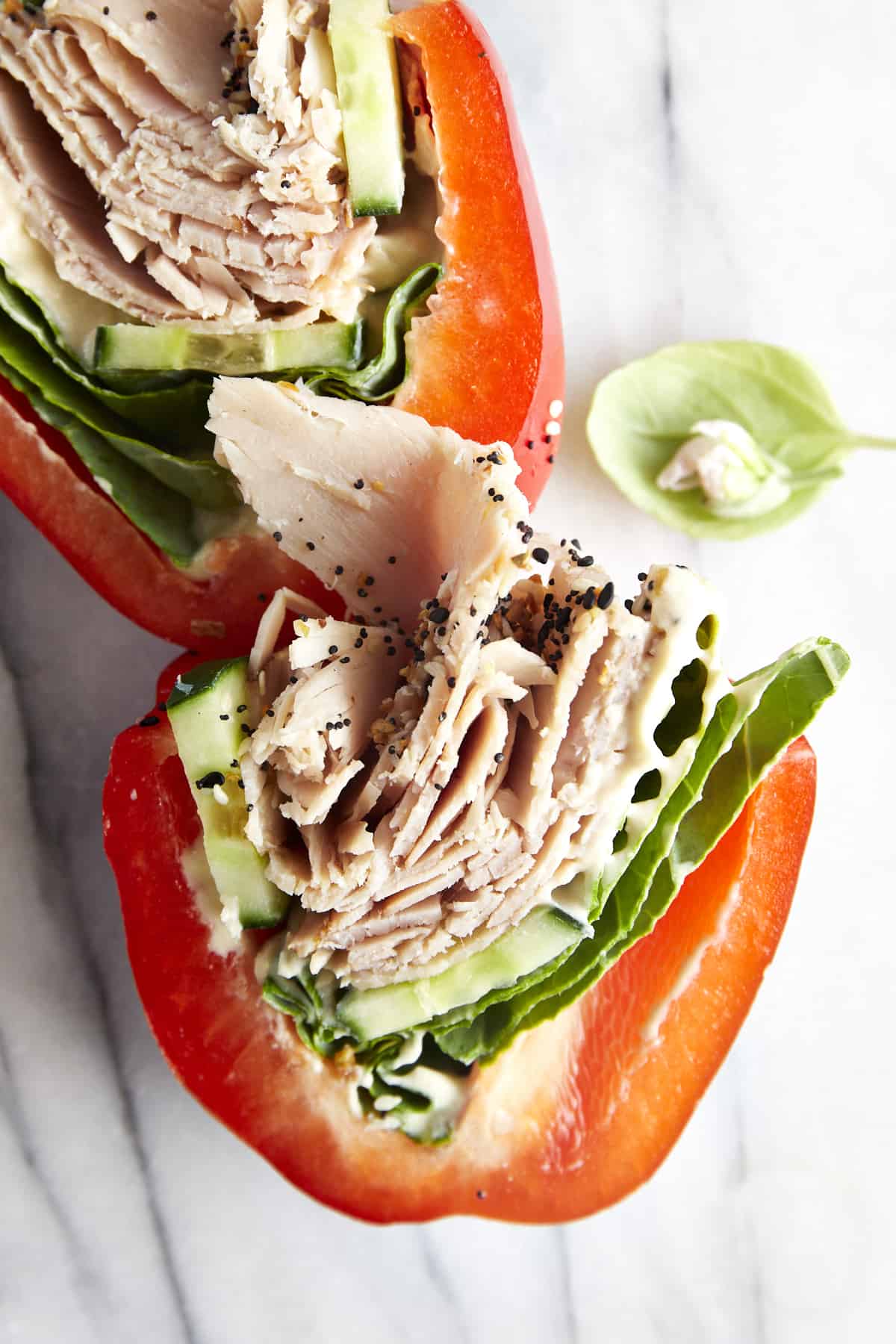 Overhead image of a sliced bell pepper sandwich with hummus, lettuce, cucumber, and turkey. 