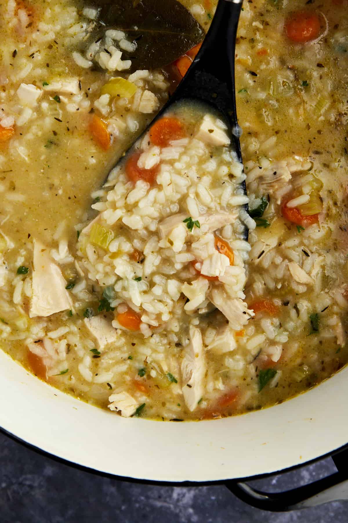 A ladle lifting a portion of chicken and rice soup from a pot. 