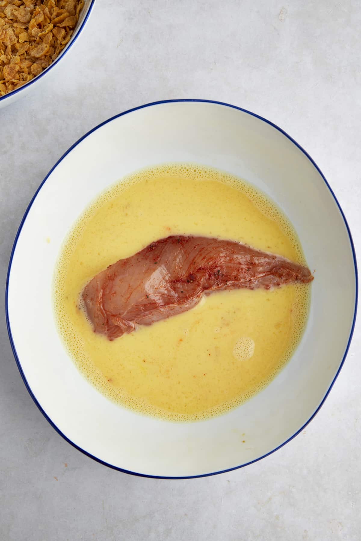 Raw seasoned chicken in a bowl of egg wash.