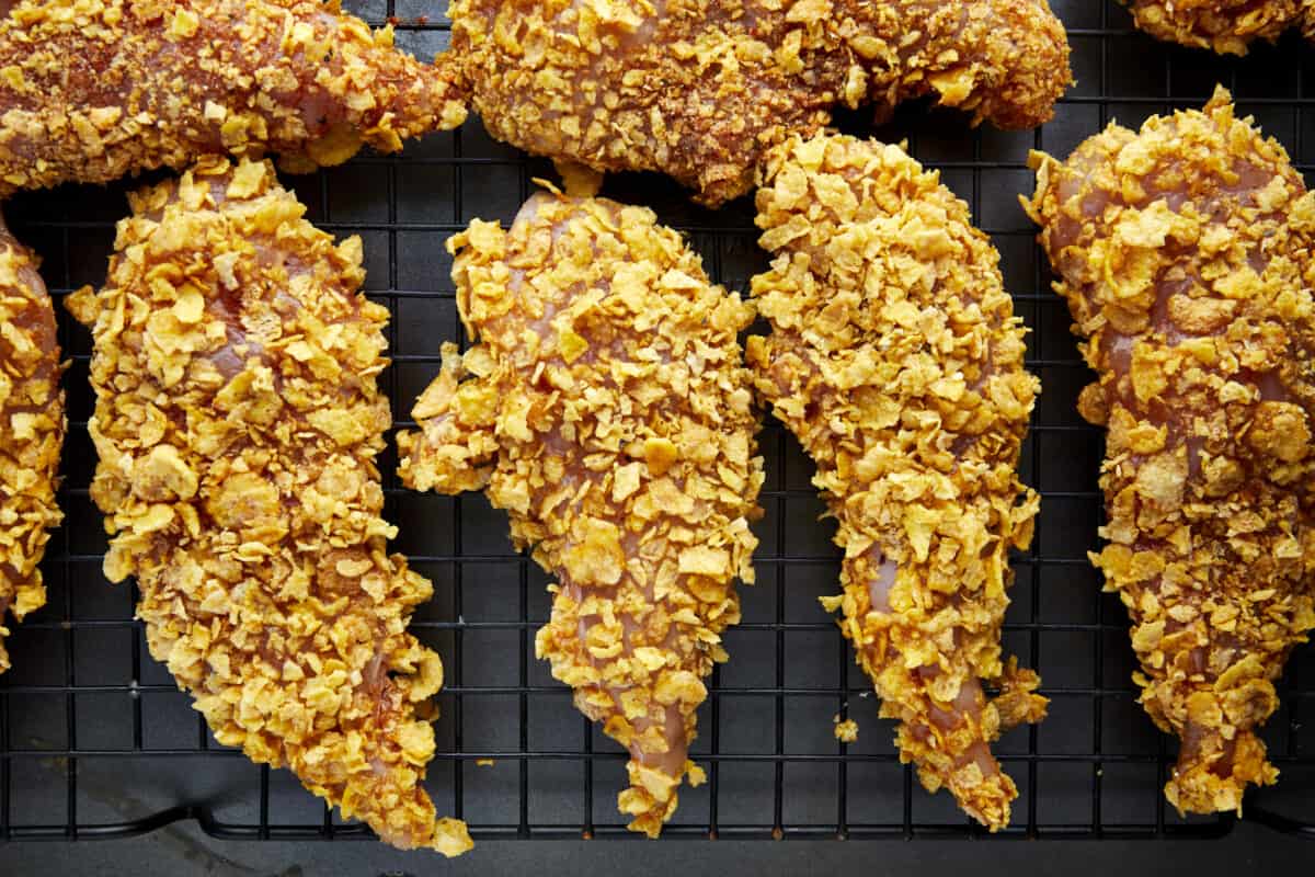 Unbaked cornflake chicken tenders on a wire rack over a baking sheet. 