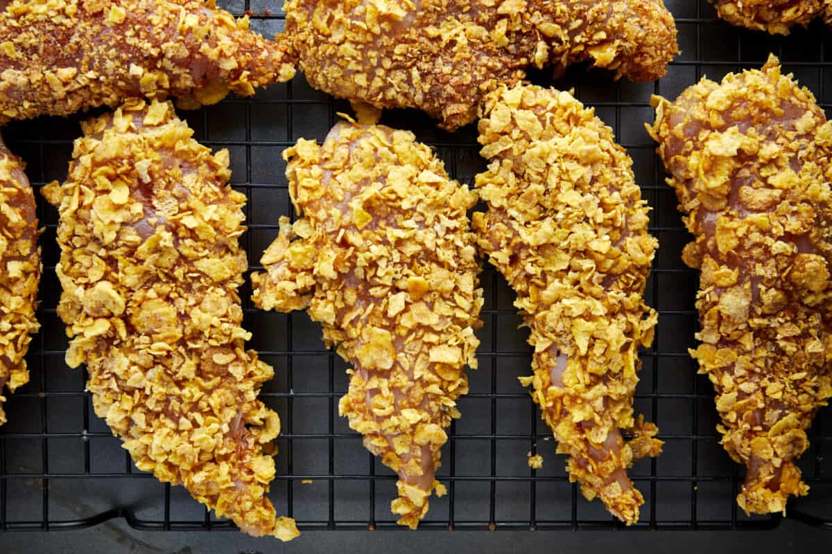 Unbaked cornflake chicken tenders on a wire rack over a baking sheet.