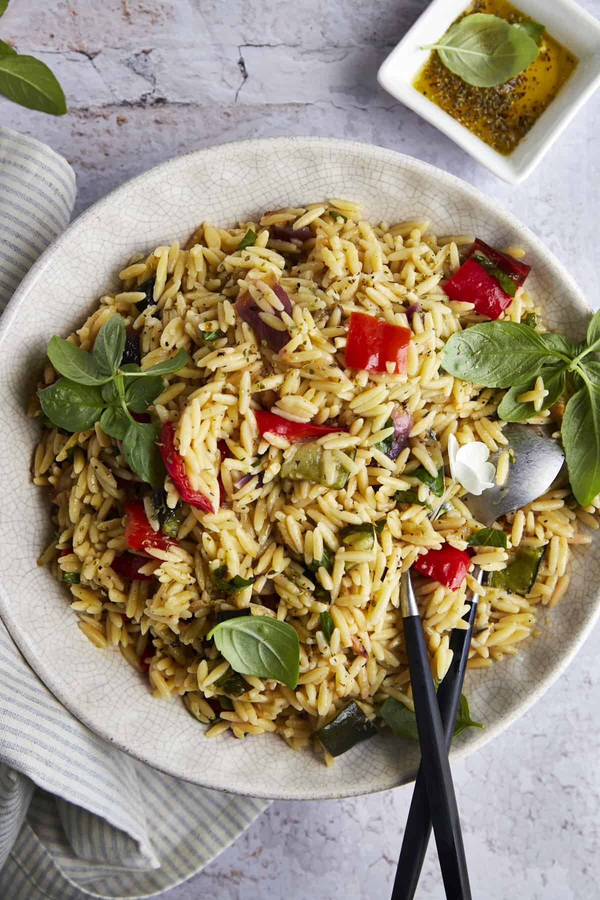 A bowl of roasted veggie pasta salad with serving spoons on top. 