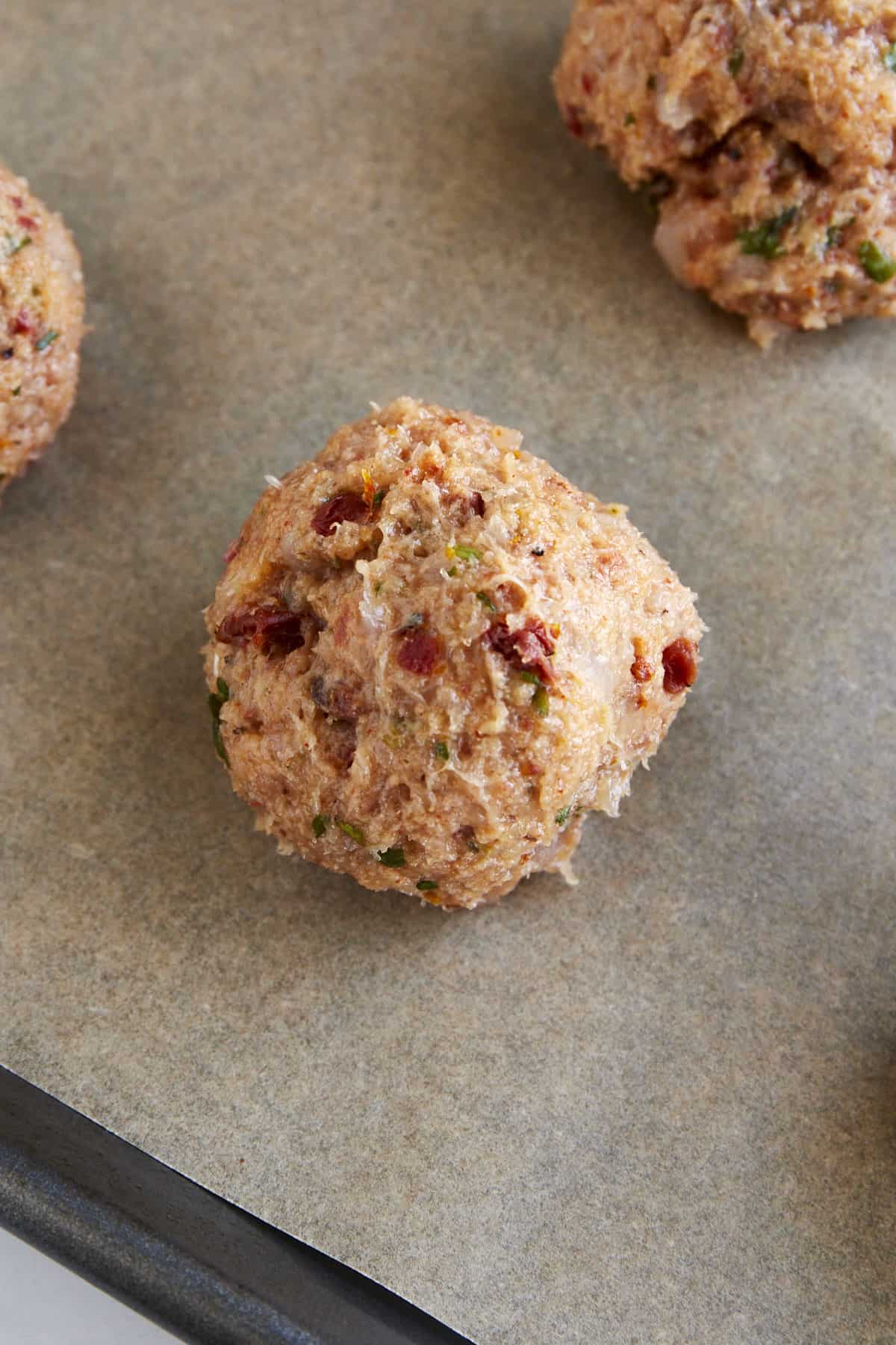 Raw ground chicken meatballs on a parchment paper-lined baking sheet. 