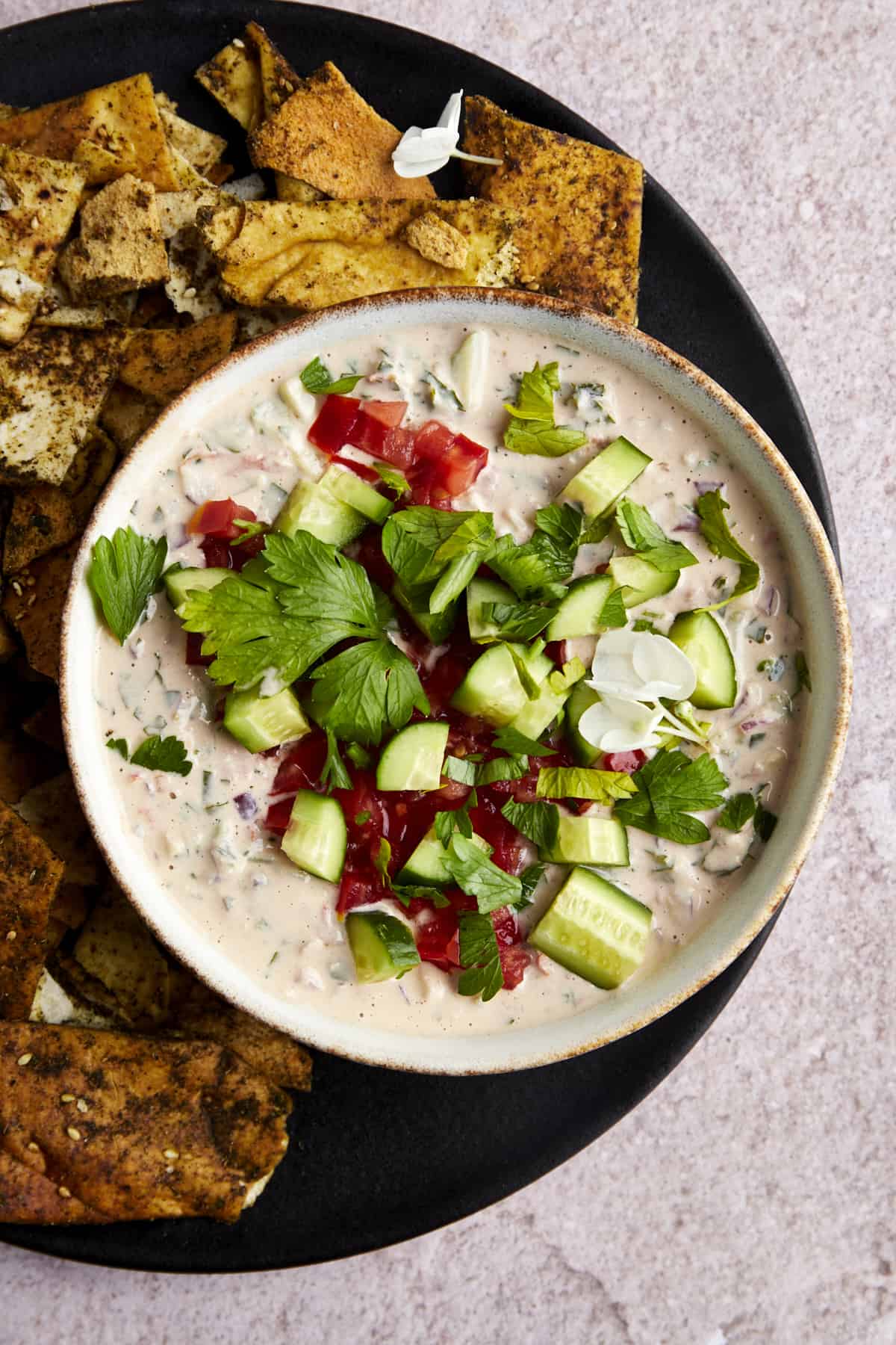 A bowl of cucumber tomato tahini salad with a side of pita chips. 