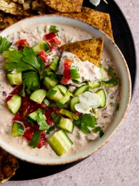 A pita chip dipping into a bowl of tahini salad.