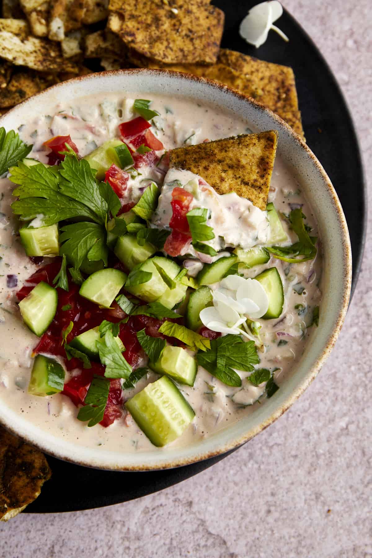 A pita chip dipping into a bowl of cucumber tahini salad. 