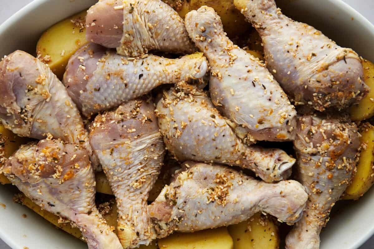 Raw chicken drumsticks over potatoes in a baking dish. 