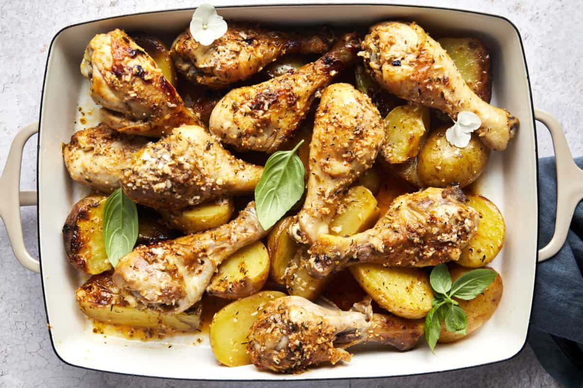 Baked garlic parmesan chicken drumsticks and potatoes in a baking dish. 