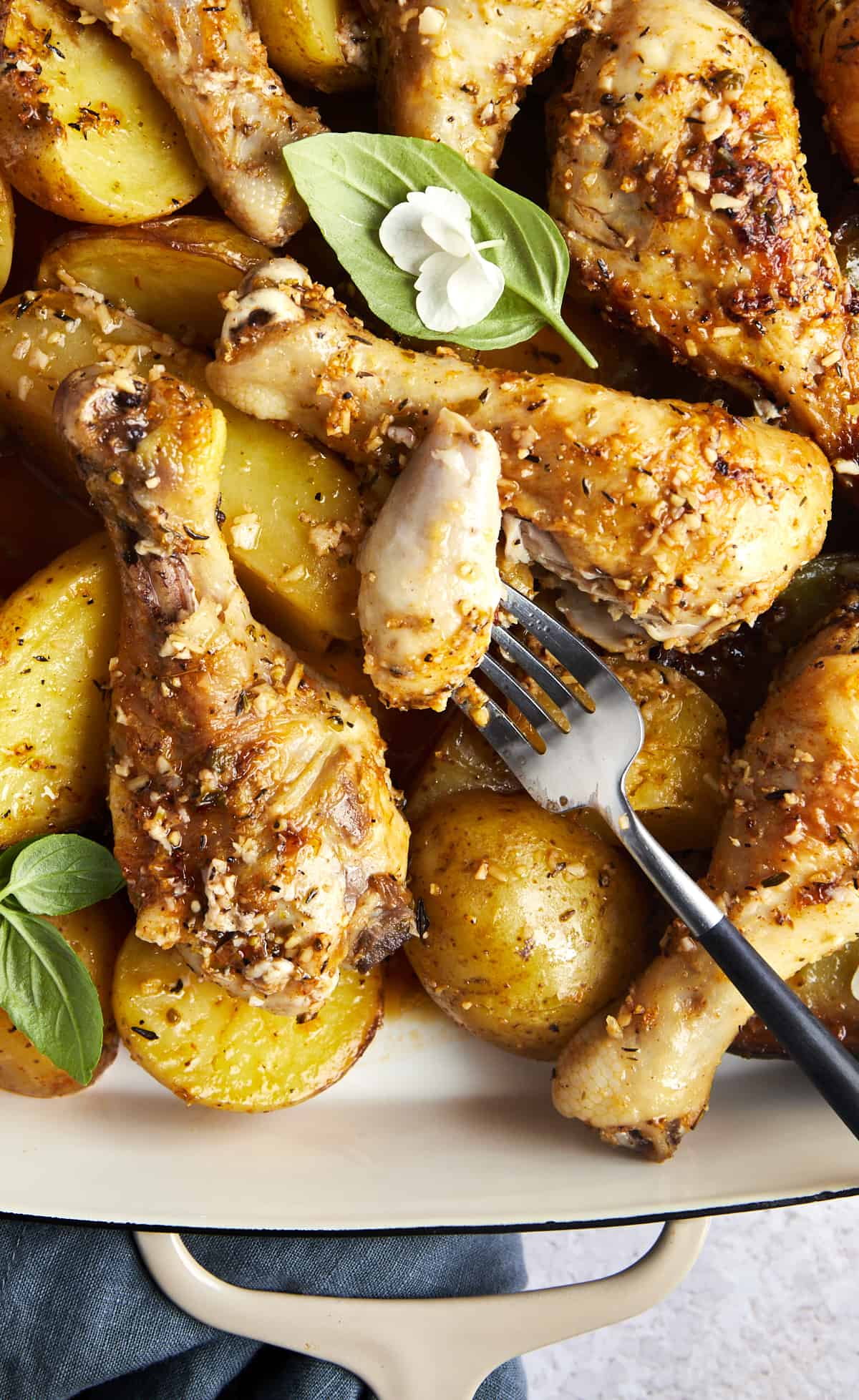 A fork holding a bite of chicken over a pile of parmesan chicken drumsticks and potatoes.