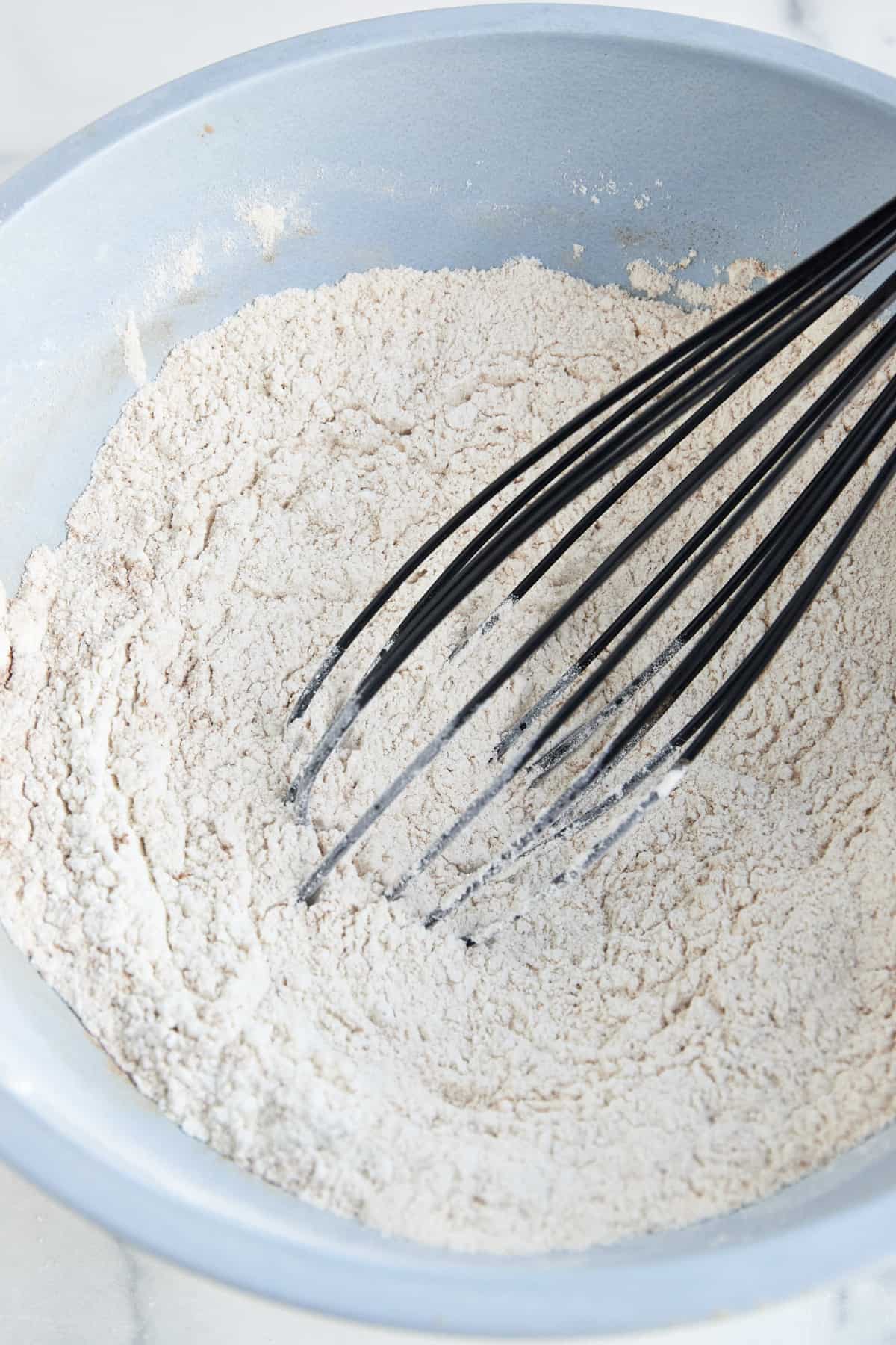 Dry muffin batter ingredients being whisked in a blue bowl. 