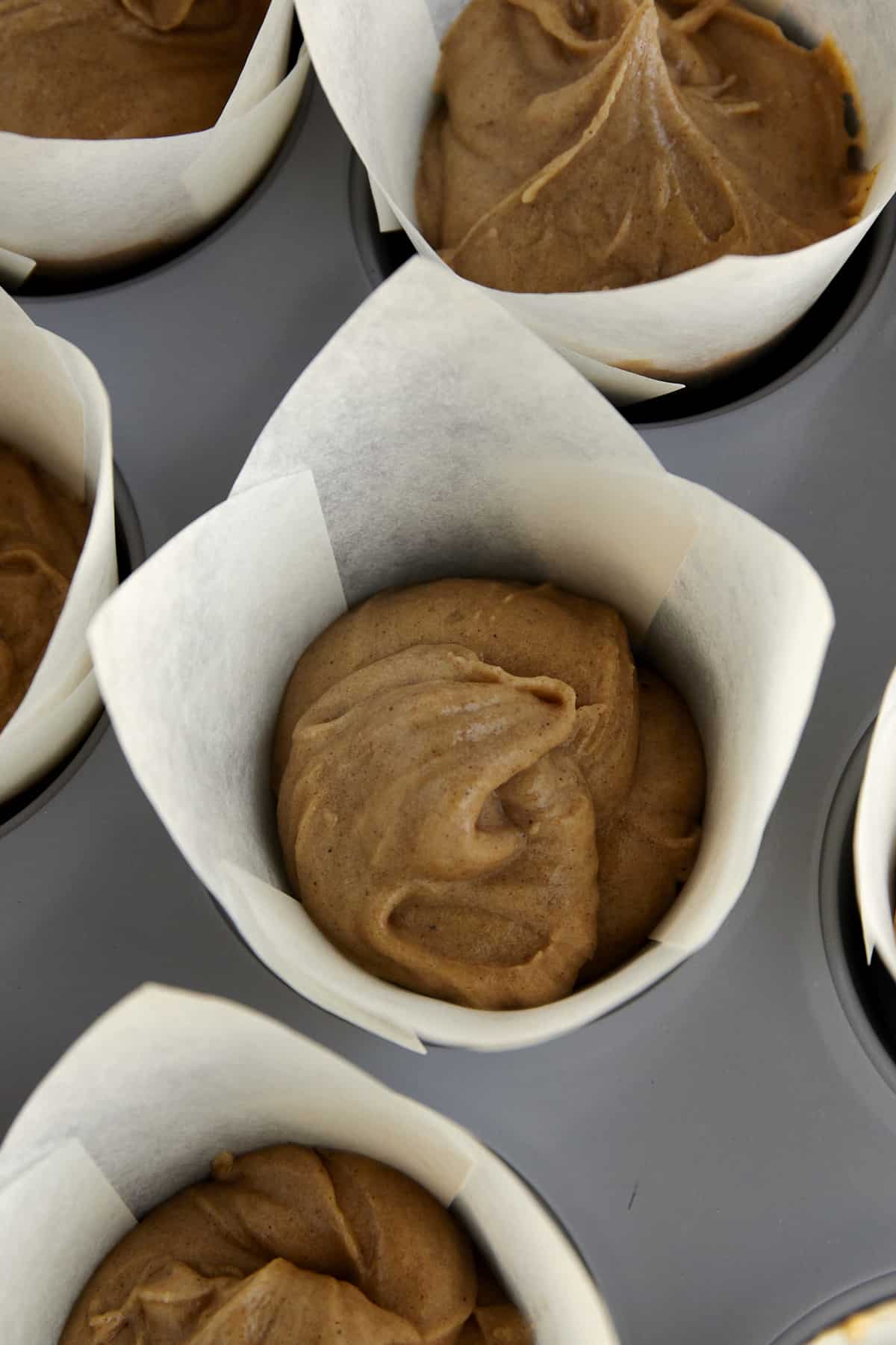 Unbaked apple cider muffins in a muffin tin lined with paper. 