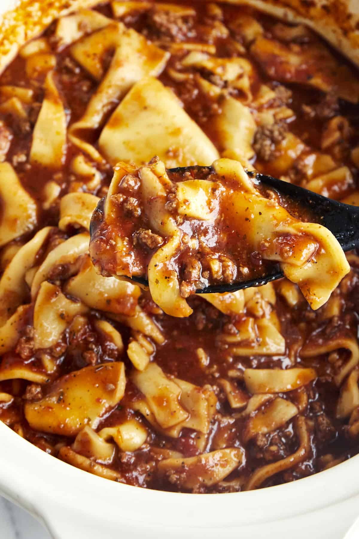 A spoon lifting a bite of lasagna soup from a crockpot. 