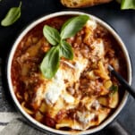A spoon sticking out of a bowl of lasagna soup topped with fresh basil.