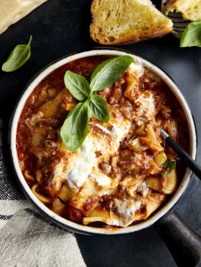 A spoon sticking out of a bowl of lasagna soup topped with fresh basil.