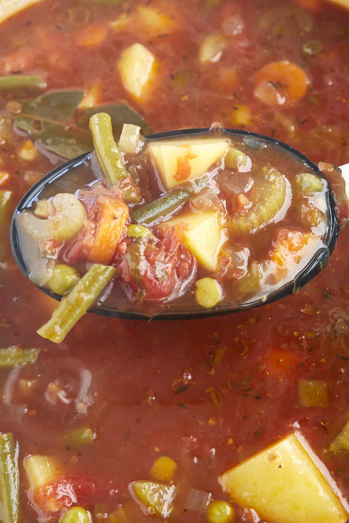 A spoon scooping up slow cooker vegetable soup. 
