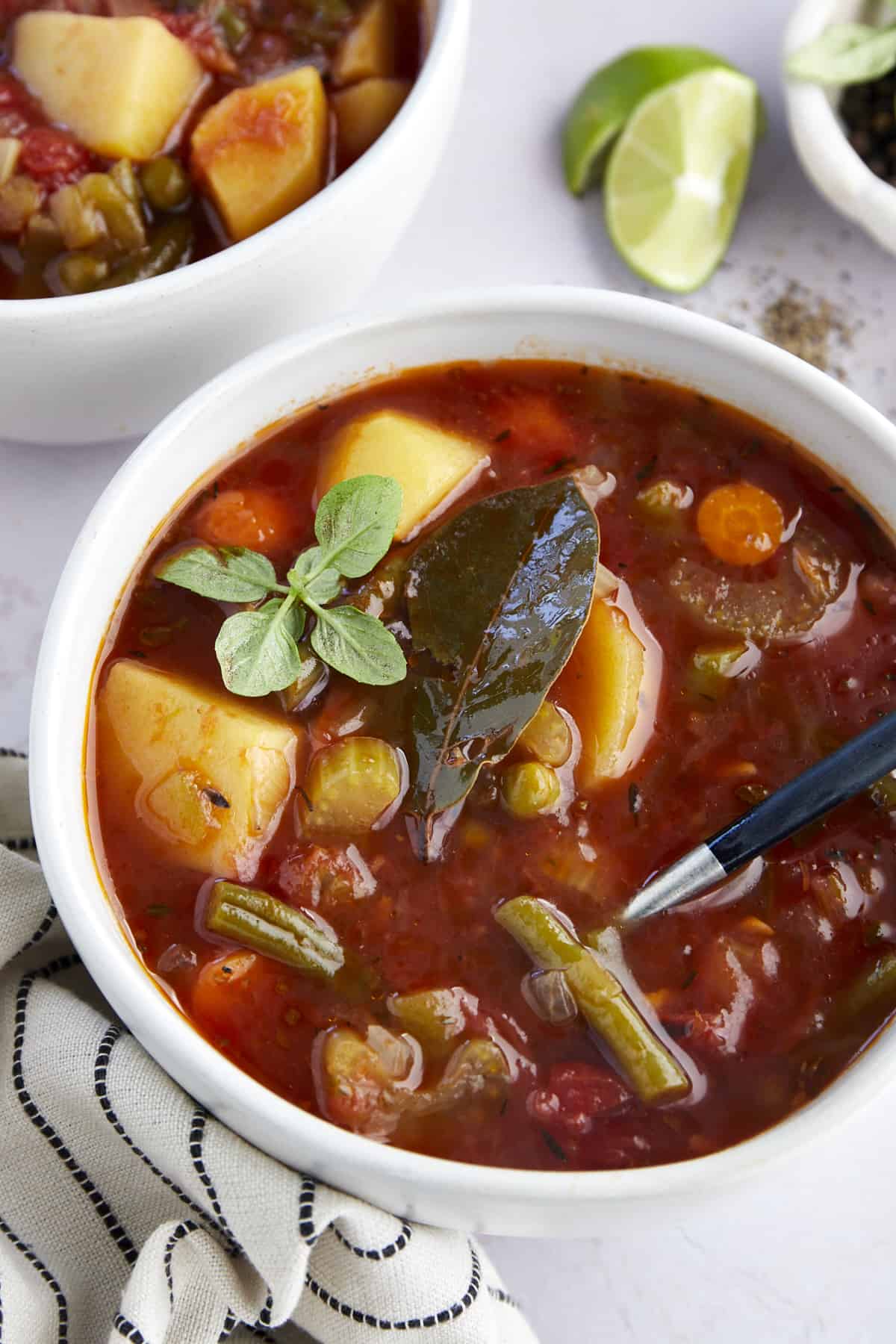 Close up image of a bowl of slow cooker vegetable soup topped with a bay leaf and greens. 