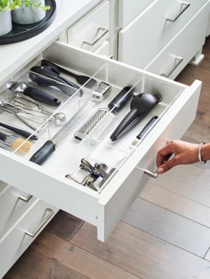 A kitchen drawer with organized utensils in a clear container.