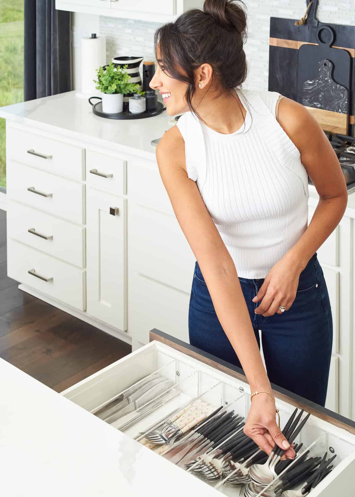 smiling woman placing spoons in drawer organizer of open drawer.