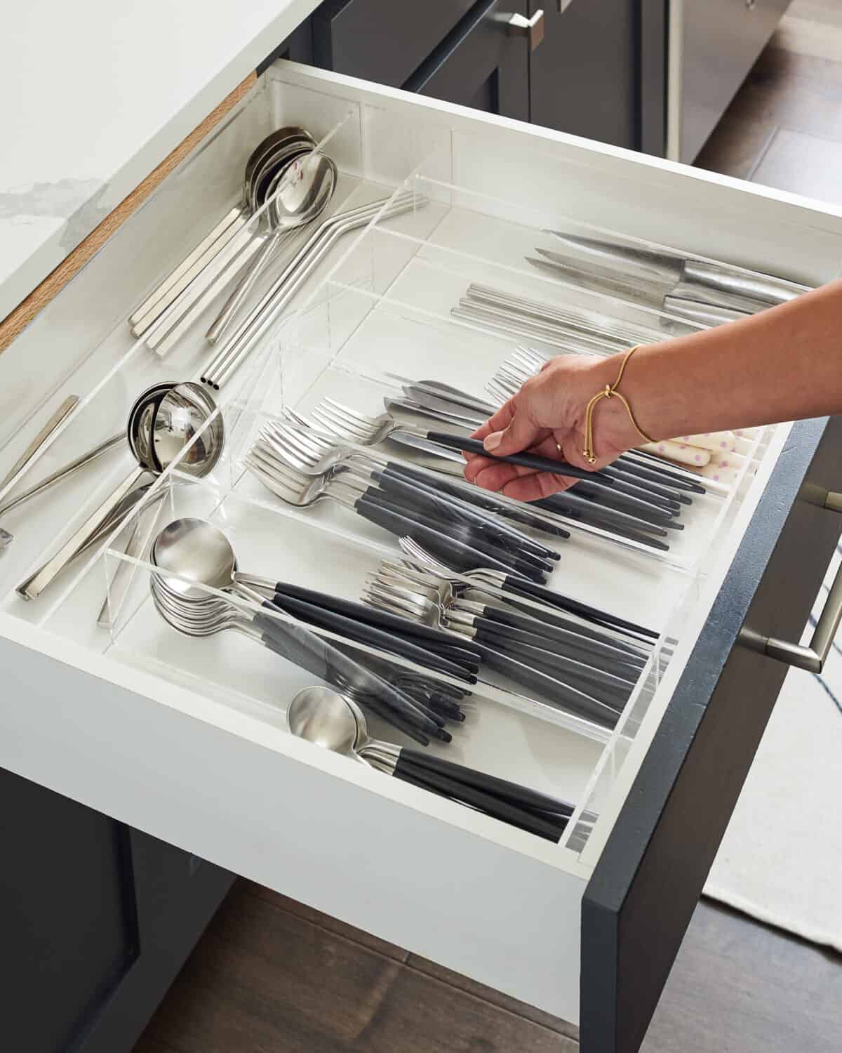 A hand placing a fork in a silverware drawer organized with a custom storage container. 