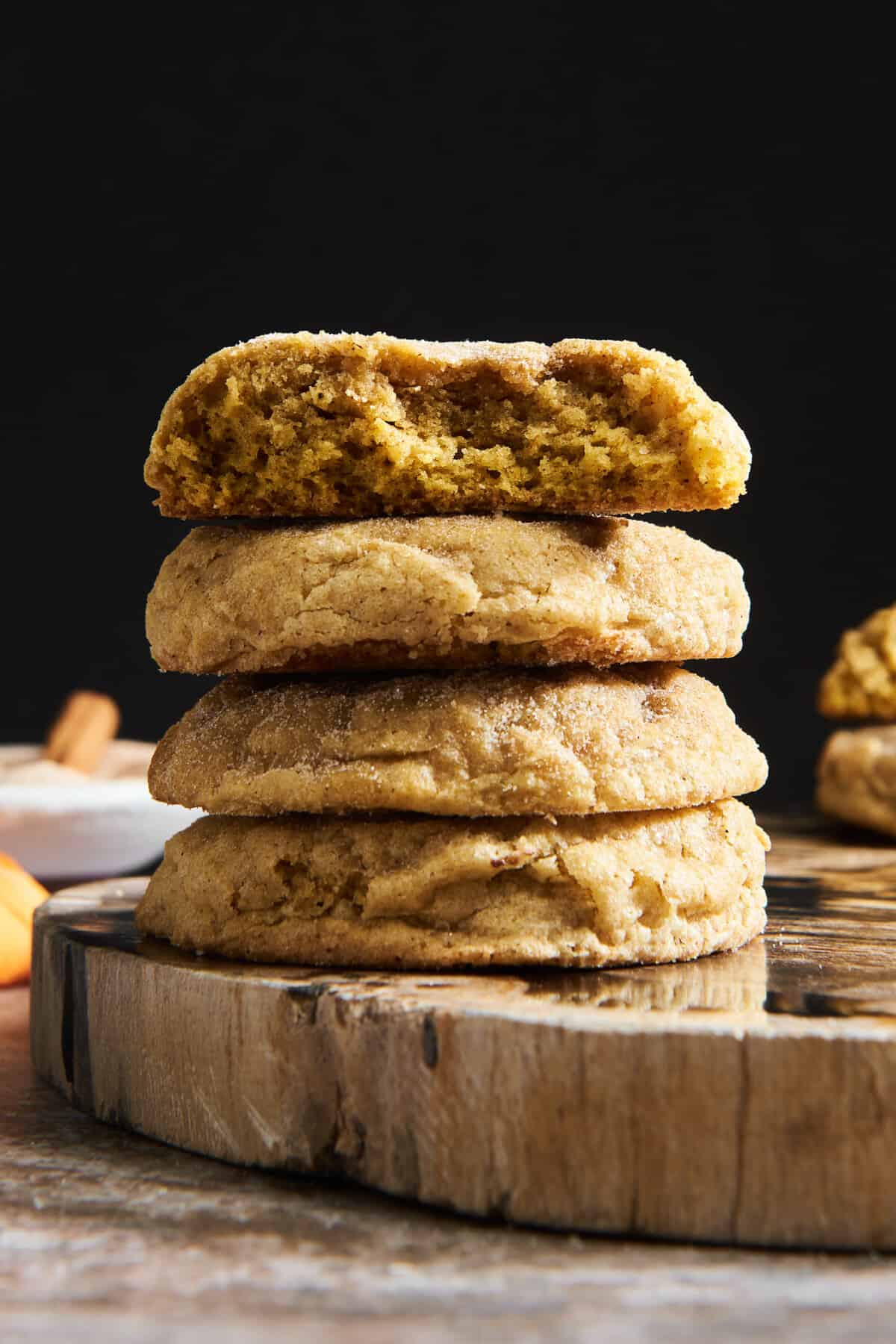 A stack of four sugar coated pumpkin cookies, the top one missing half. 
