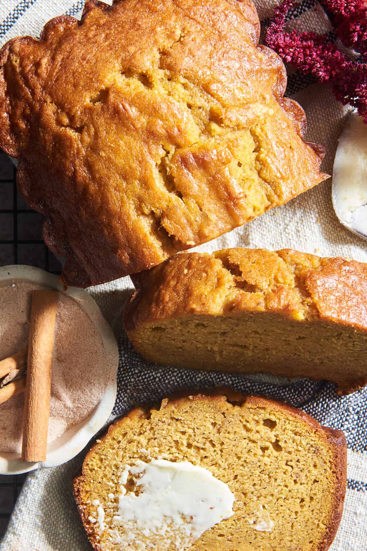 A loaf of pumpkin banana bread with two slices cut and one topped with butter. 