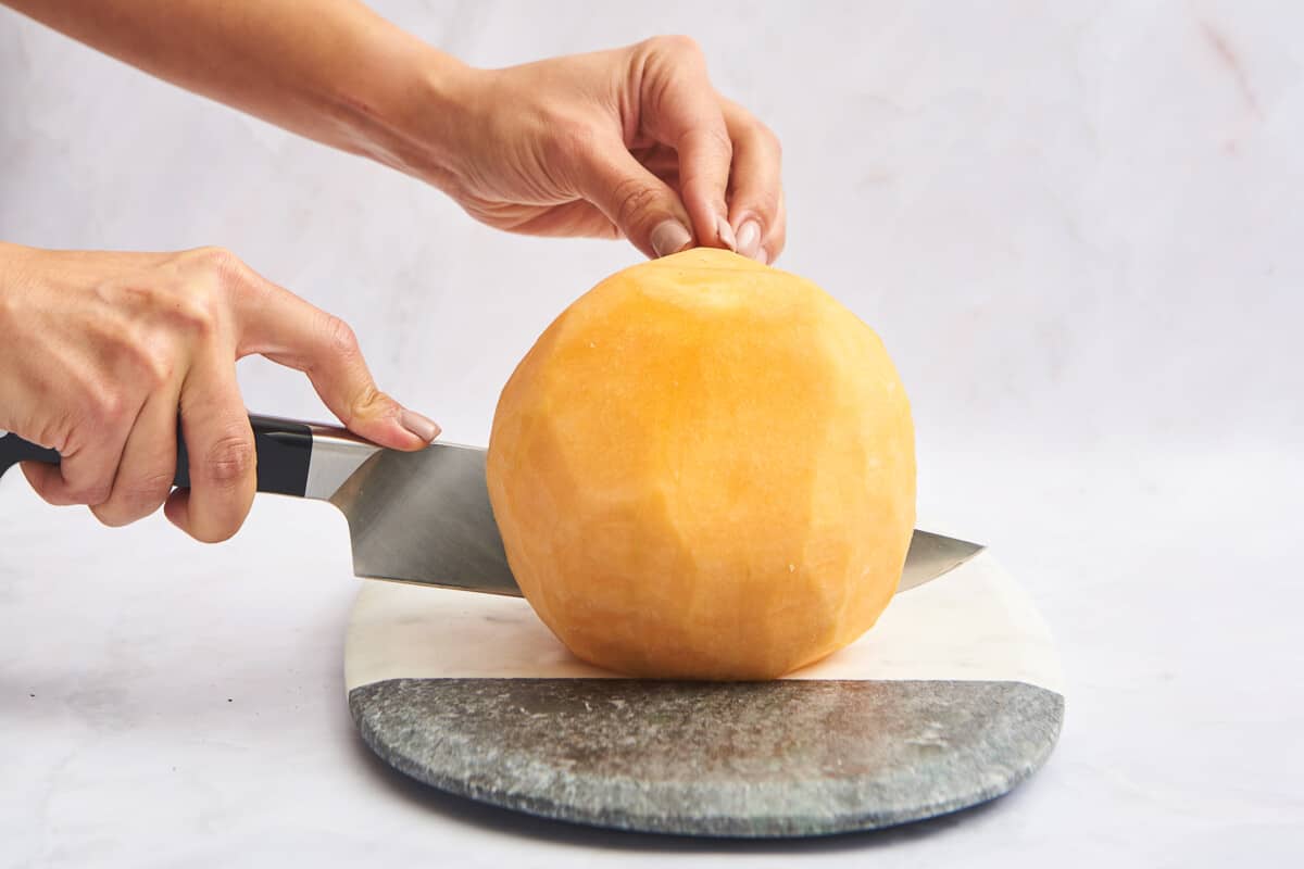 A peeled cantaloupe being cut in half. 