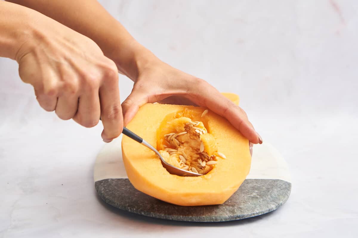 A spoon scooping the seeds from a cantaloupe half. 