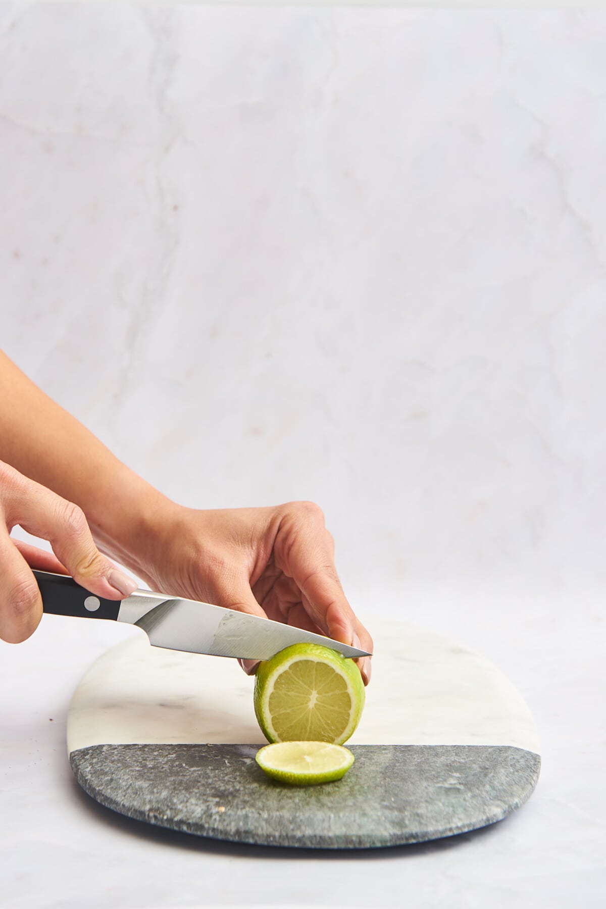 A lime being sliced into rounds on a marble cutting board. 