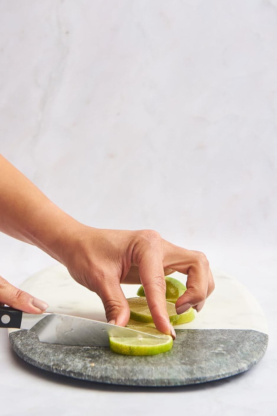 Lime rounds being sliced in half on a marble cutting board. 