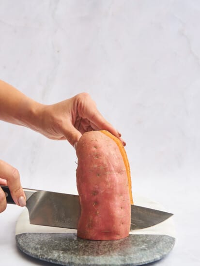 A sweet potato being sliced in half lengthwise.