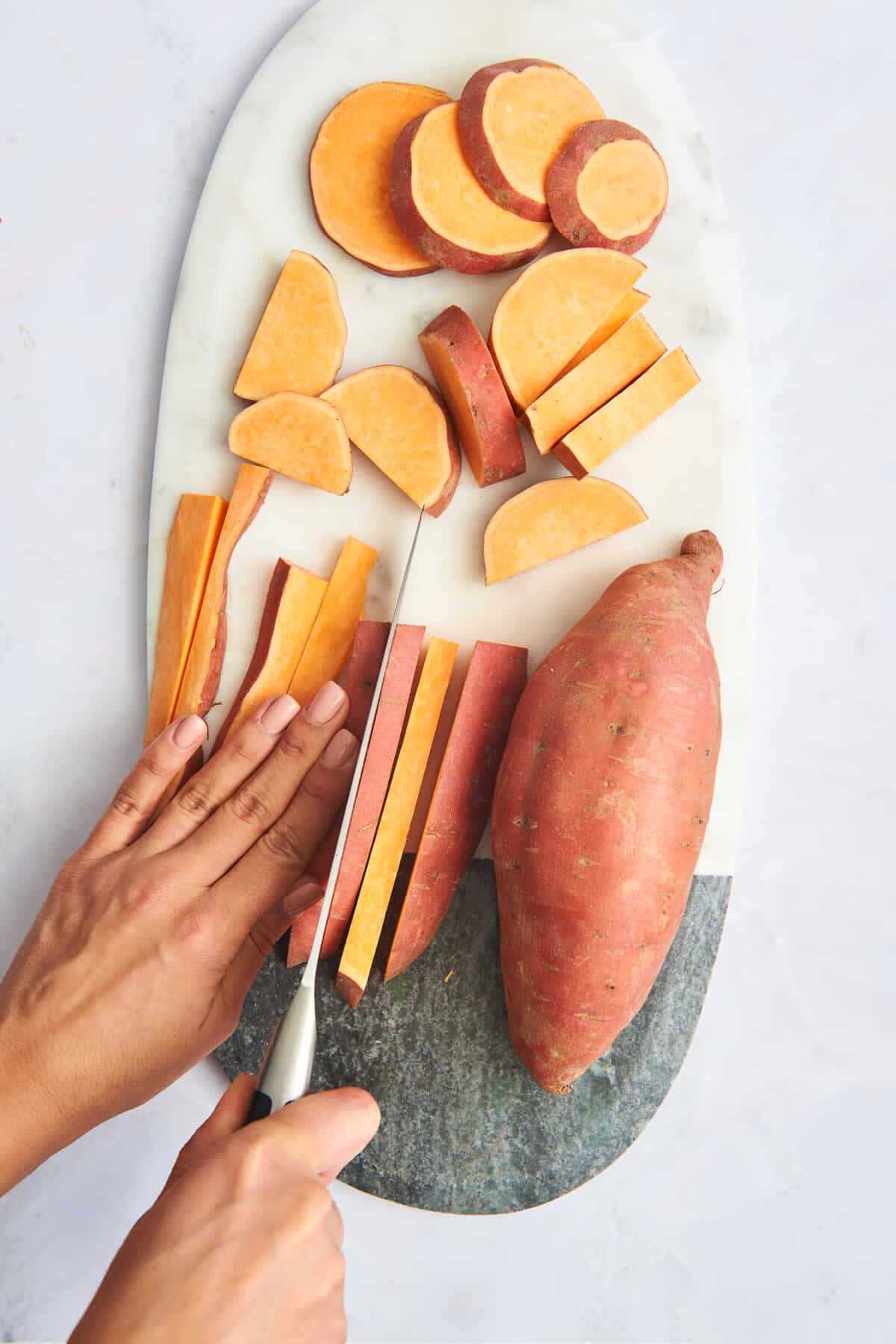 Rounds and quarters of sweet potato next to a whole sweet potato and one being sliced into sticks. 
