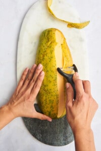 A vegetable peeler being used to remove the skin of a papaya.