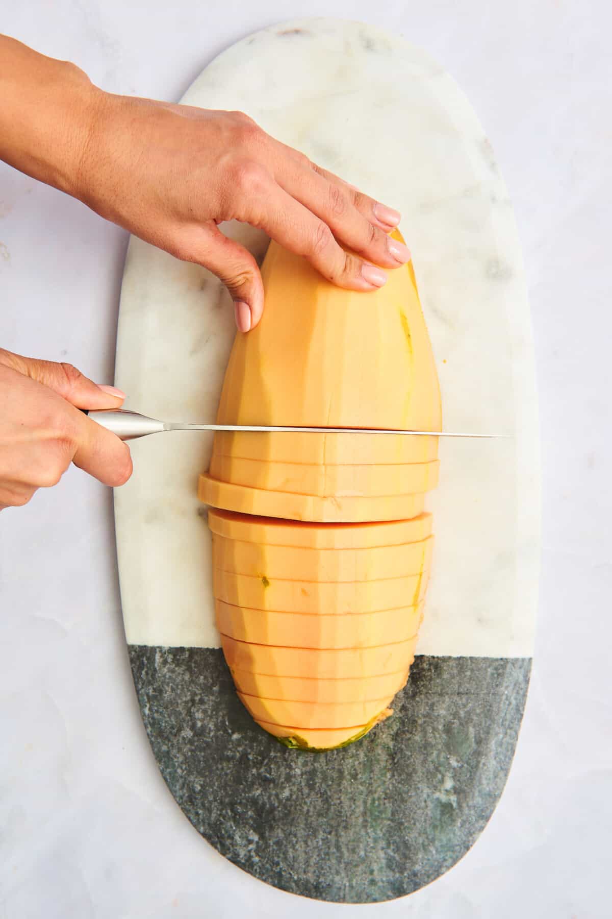 A hand slicing a papaya into half rings.