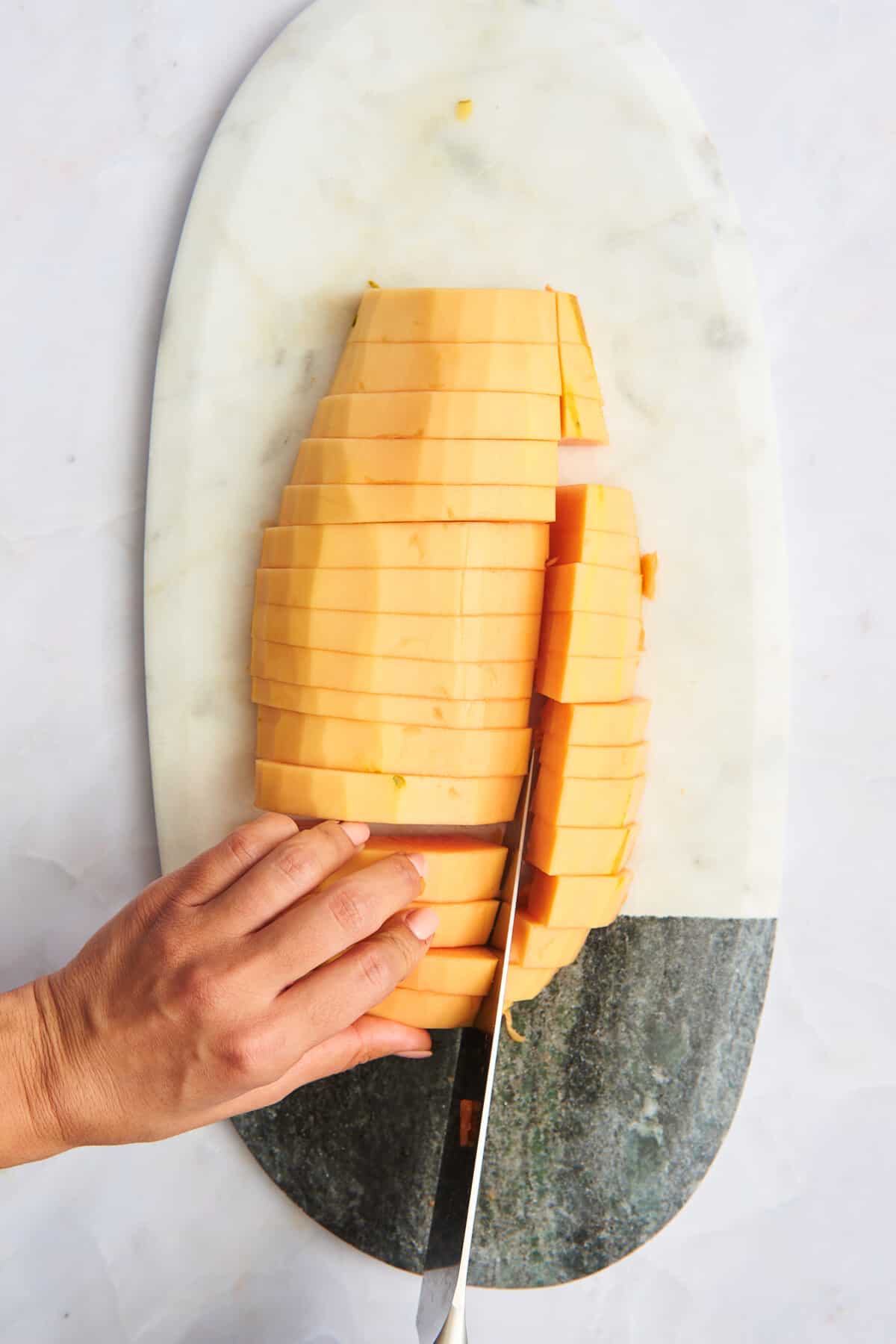 A hand slicing papaya pieces into cubes. 