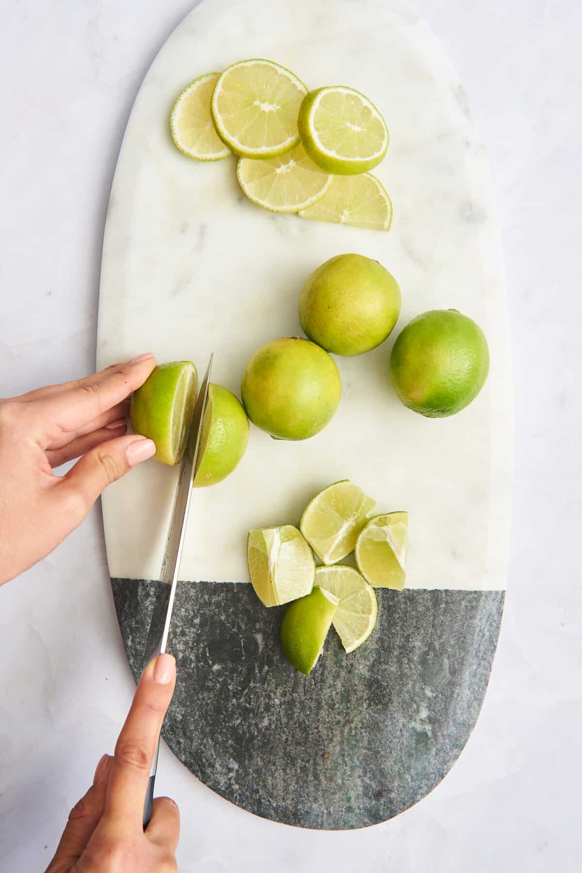 Lime rounds, whole limes, lime wedges, and a lime being halved on a cutting board. 
