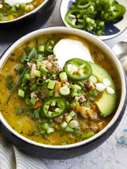 A bowl of healthy white turkey chili topped with sour cream, avocado, jalapeños, and scallions.