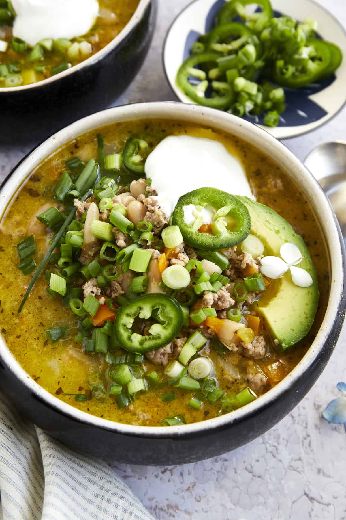 A bowl of healthy white turkey chili with scallions, jalapeño, avocado, and sour cream. 