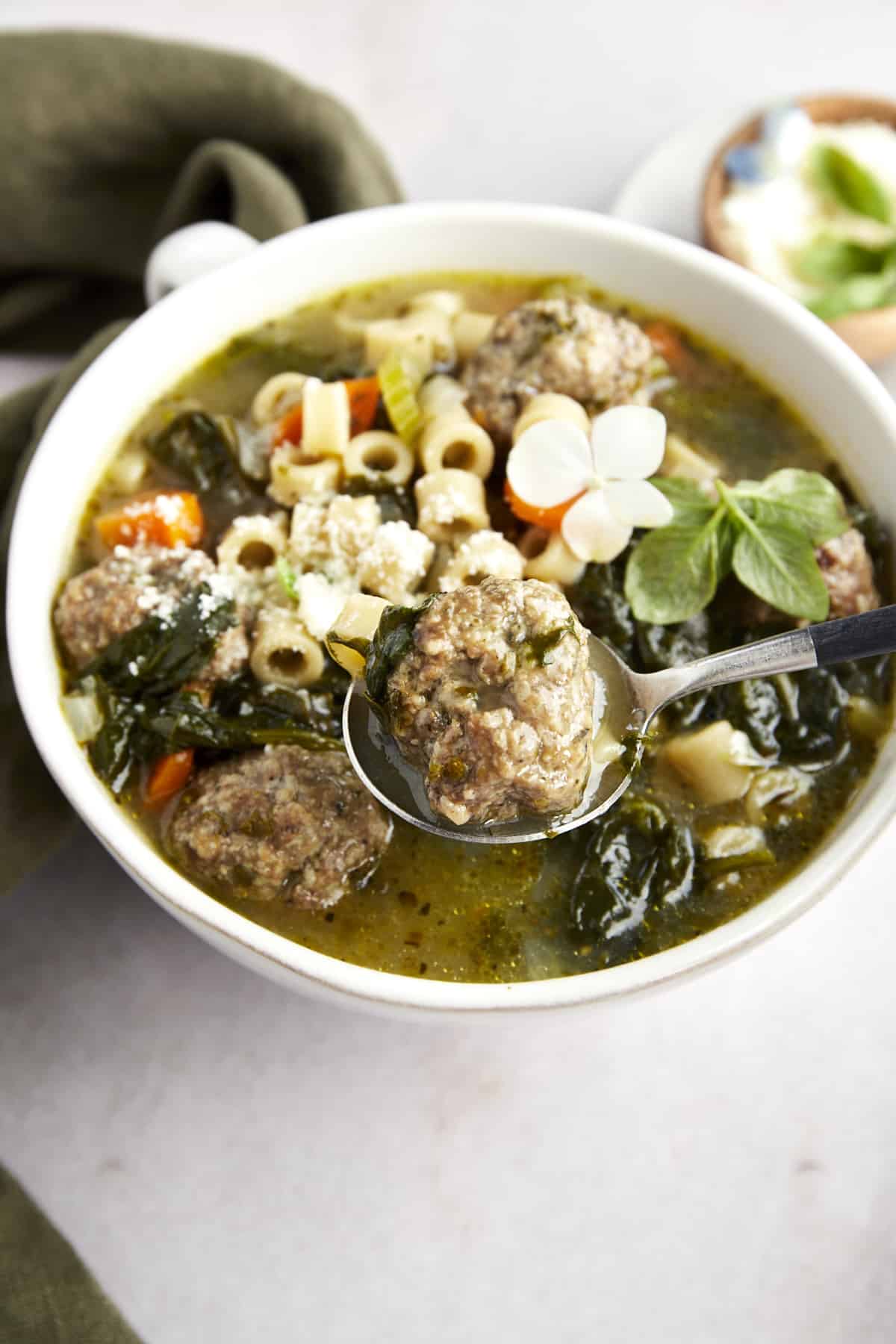 A spoon lifting up a beef meatball from a bowl of Italian wedding soup. 