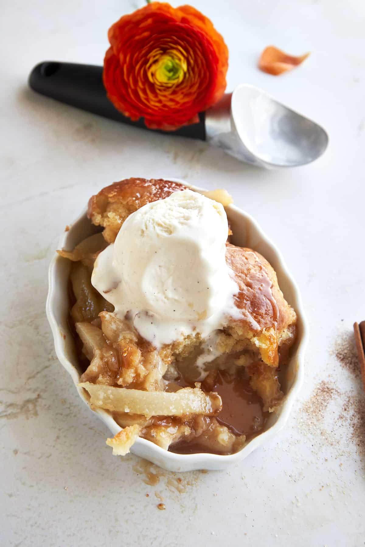 A serving of pear cobbler in a dish topped with vanilla ice cream with a bite missing. 