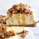 A slice of baklava cheesecake being lifted from a cake stand.